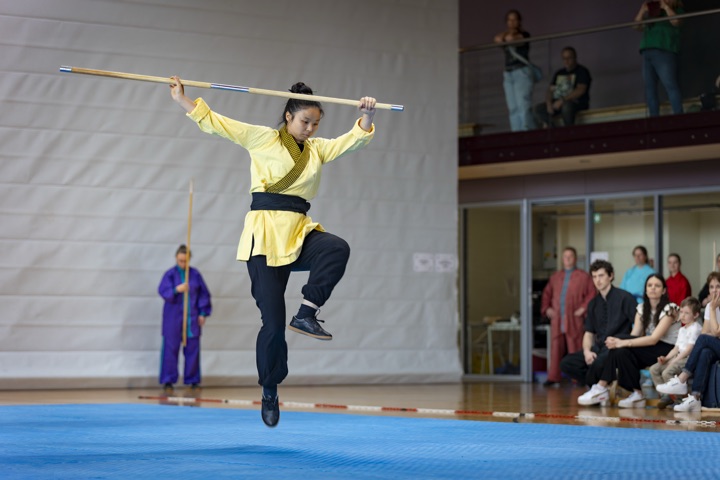 一名选手身著黄衣，平持长棍腾空而起